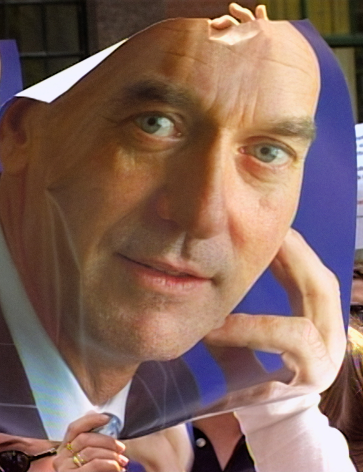 A poster of a white bald freshly-shaven man is being held up by a crowd