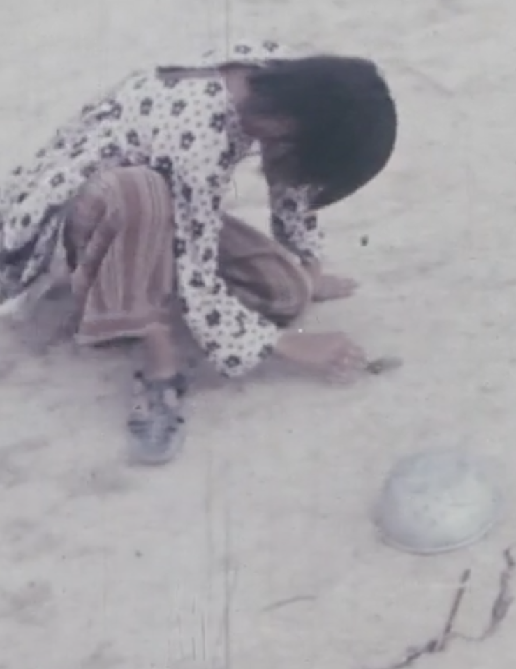 Young girl in floral top crouched over barren ground