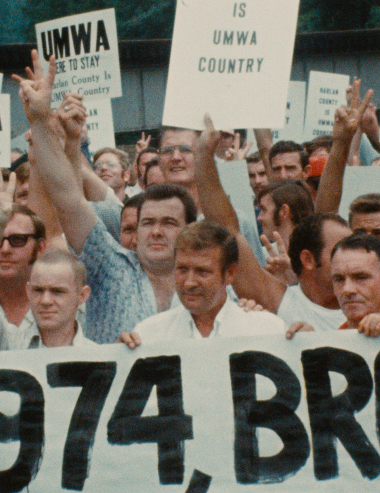 A crowd of white men holding signs promoting "UMWA" and raising arms