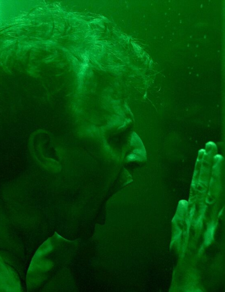 A white man presses against glass and screams, lit in bright green
