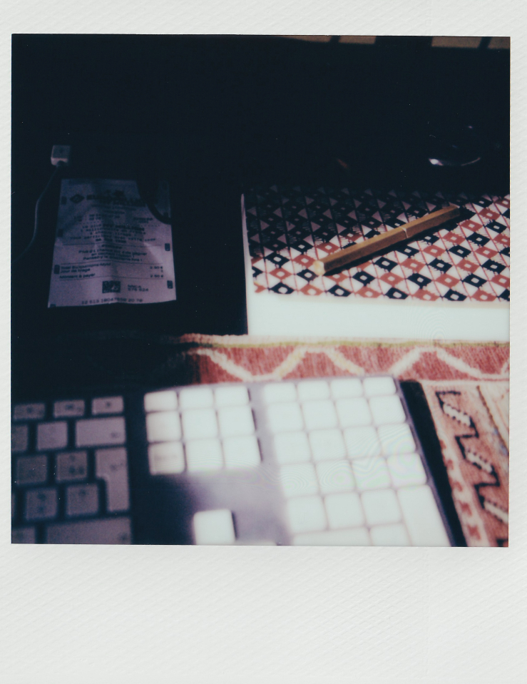 Close up Polaroid of a keyboard on an Armenian rug and a mosaic patterned notebook with a pencil on top